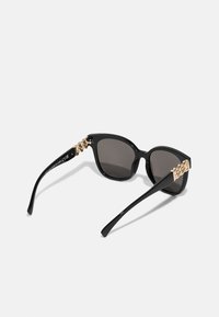 Black sunglasses with cat-eye shape, dark lenses, and gold-tone metal detailing on the arms. Smooth finish and sleek design.