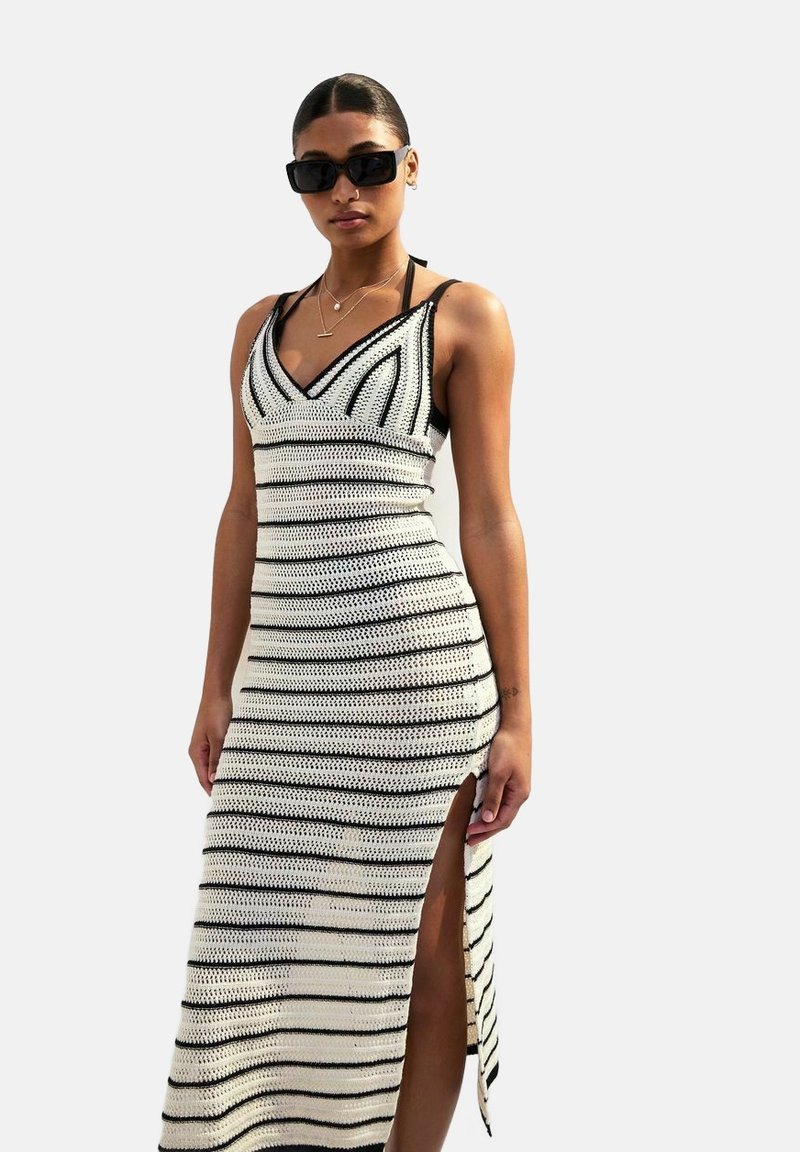 Maxi abito lavorato a maglia bianco con righe orizzontali nere, caratterizzato da una scollatura a V e una spacco laterale per un tocco di originalità. Realizzato in materiale elasticizzato.