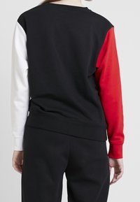 Black sweatshirt with multicolored sleeves: left in white, right in red. Features a ribbed neckline and cuffs, soft cotton fabric.