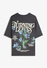 Tricou din bumbac gri închis cu un design grafic floral, având flori albastre, text crem și un aranjament stratificat al textului pe spate.