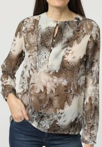 Blusa de patrones florales en tonos marrón y crema, con cuello redondo, abertura en el frente, mangas largas y tela ligera, con sutiles detalles de textura.