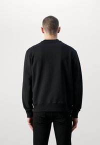 Svart sweatshirt med rund halsringning, ribbade muddar och fåll. Mjuk textur, enkel design. Buren med svarta jeans. Enfärgad bakgrund.