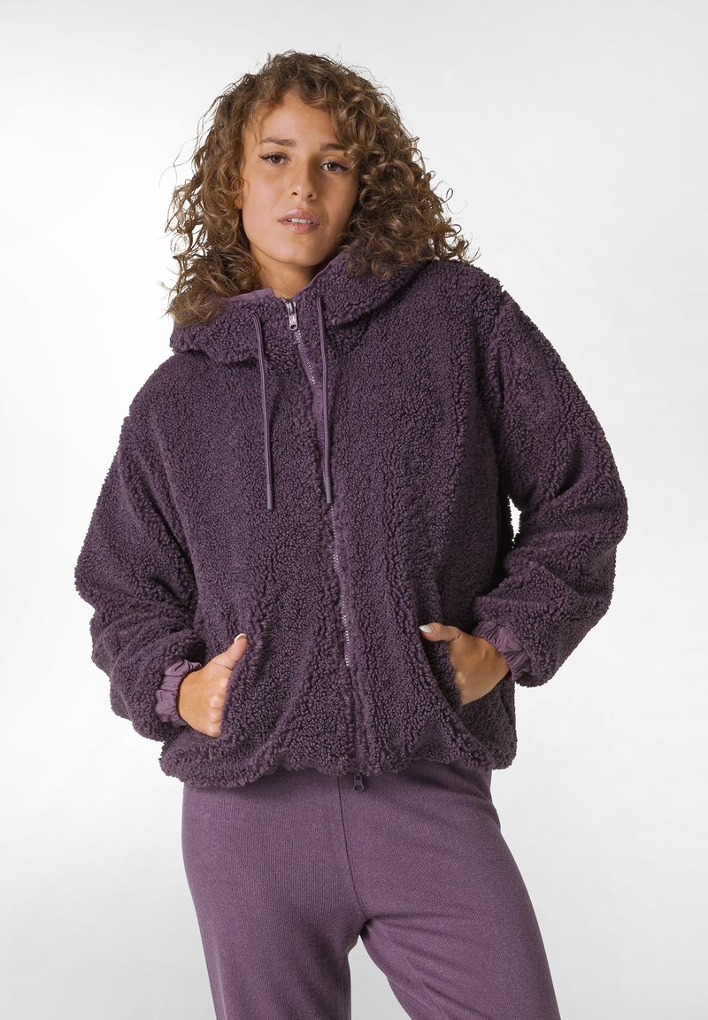 Hanorac oversized din fleece violet, cu un finisaj texturat, glugă, fermoar frontal și buzunare laterale. Mâneci lungi cu manșete elastice. Pantaloni asortați.