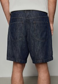 Shorts din denim, de culoare albastru închis cu dungi verticale, croi normal, lungime până la mijlocul coapsei, cu două buzunare la spate și cusături întărite.