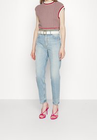 Stickad ärmlös topp i röd och vit med ett texturerat mönster, kombinerad med ljusblå höga jeans och rosa remsandaler med klack.