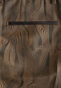 Tissu marron et noir avec un motif ondulé rappelant un veinage de bois et une poche passepoilée noire étroite et horizontale, centrée près du haut.