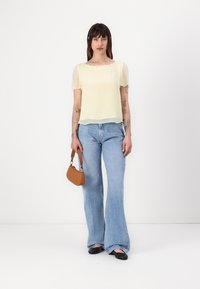 Haut transparent jaune à manches courtes, associé à un jean léger évasé bleu clair. Tient un petit sac à main marron. Tissu lisse avec une coupe décontractée.