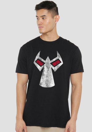 Junger Mann mit kurzen Haaren, der ein schwarzes T-Shirt mit einem großen weißen und roten abstrakten geometrischen Gesichtsmotiv trägt.