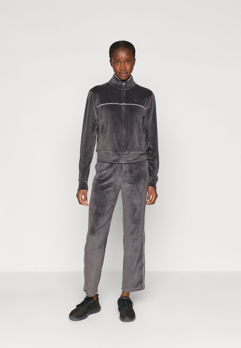 Tuta in velluto grigio con giacca con zip e pantaloni con vita elastica, caratterizzata da strisce laterali bianche e un piccolo logo sul petto.