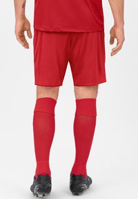 Rote Sportshorts, passende rote kniehohe Socken mit Netzstruktur und schwarze Fußballschuhe. Einfaches Design ohne Verzierungen.