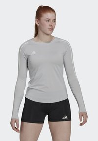 Hellgraues langärmliges Sportshirt mit weißen Akzenten und Rundhalsausschnitt. Schwarze Shorts mit einem weißen Logo am Oberschenkel. Glattes, eng anliegendes Material.