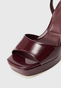 Burgundy lackläder högklackad sandal med öppen tå, bred rem över framfoten och tjock plattformsula. Slät, glänsande yta.