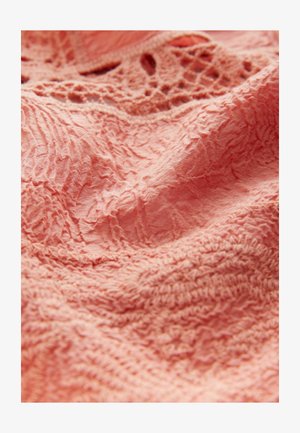 Texturerad tyg i mjuk korallfärg, med intrikata broderier och en rynkad effekt, som framhäver djup och detalj i designen.