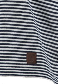 Tejido de punto a rayas horizontales en azul marino y blanco con una pequeña etiqueta de parche de cuero marrón cosida que muestra el texto y el logotipo de "KEY LARGO".