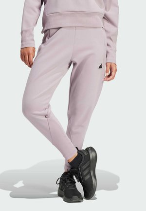 Helle lavendelne Jogginghose aus weichem Material mit einem schlanken Design und elastischen Bündchen, kombiniert mit schwarzen Sportschuhen. Schwarzes Logo-Detail sichtbar.
