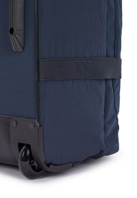 Navy blue wheeled suitcase with a textured fabric body, reinforced black plastic base, and a sturdy black strap for added support.