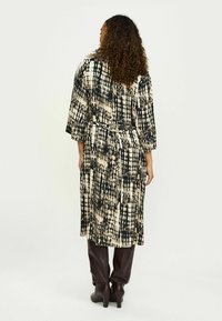 Pikk, mustriline kleit, millel on must ja kreem värv, vöökoht on rõhutatud. Lõdvad varrukad ja voolav disain, sobitatud pruuni pükste ja kontsakingadega.