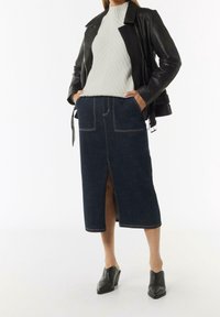 Jupe en denim avec fente avant, couleur bleu foncé, couture contrastante et deux poches. Associée à un pull léger texturé et une veste en cuir noire.