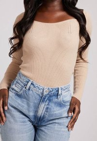 Haut beige à manches longues côtelé avec un décolleté carré, associé à un jean en denim taille haute bleu clair à finition délavée et poches avant.