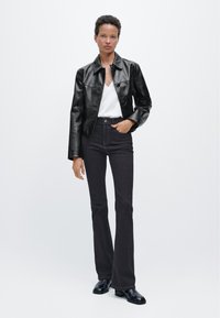 Černá kožená krátká bunda přes bílý top s výstřihem do V, doplněná vysokým pasem tmavých džínů s rozšířenými nohavicemi a černými kotníkovými botami.