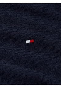 Navy gestrickter Stoff weist ein kleines gesticktes Logo mit roten, weißen und blauen Details auf, das prominent auf dem Textil dargestellt ist.