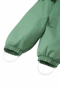 Zbliżenie rękawa zielonej, wodoodpornej kurtki z elastycznymi mankietami i białymi pętelkami do łatwego zakładania. Gładka tekstura, lekka tkanina.