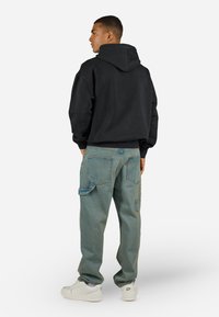 Black hoodie with a relaxed fit and a spacious hood, paired with light blue cargo jeans featuring multiple pockets and a tapered leg.