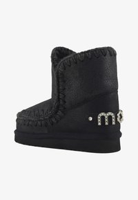 Botín de ante negro con detalle de costura, forro de peluche sintético y acentos decorativos de rhinestones en el tacón. Suela plana de goma.