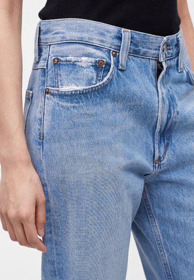 Κοντινό πλάνο ατόμου που φοράει ανοιχτό μπλε τζιν με εμφανές μπροστινό τσέπη και το χέρι να ακουμπάει δίπλα στον μηρό.
