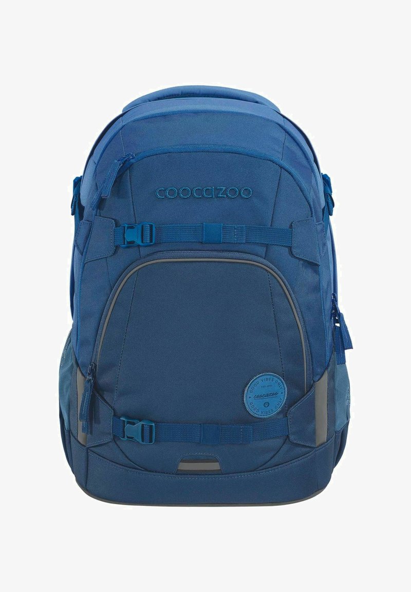 Sac à dos bleu en tissu durable, avec plusieurs poches zippées, des bretelles réglables et un badge en forme de cercle à l'avant.