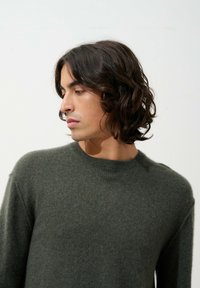 Pull en laine doux, vert foncé, avec un col rond et des poignets côtelés. Design simple, coupe légèrement ample, tissu texturé.