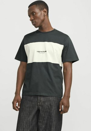 Short-sleeve t-shirt in dark green and cream with a boxy design, featuring the "Originals Studio" logo in the center. Cotton material, casual fit.
