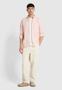 Camicia a maniche lunghe rosa chiaro sopra una t-shirt bianca, abbinata a pantaloni color crema e scarpe slip-on beige. Design semplice e classico.