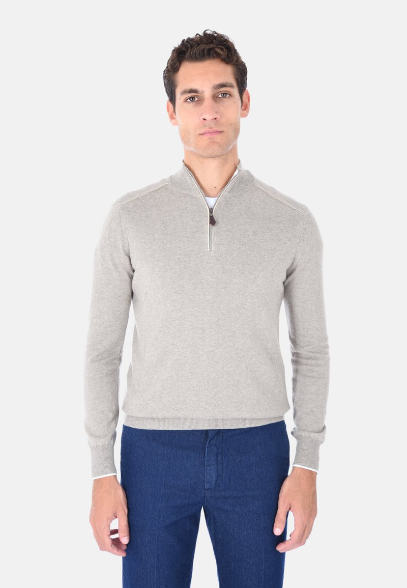 Felpa grigia chiara con zip e colletto alto, caratterizzata da cuciture a contrasto e polsini a coste, abbinata a pantaloni blu scuro.