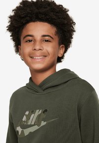 Sudadera verde de tela suave con un logotipo de Nike de camuflaje en la parte delantera. El diseño incluye una capucha doble y puños acanalados.