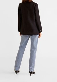 Blazer nero con vestibilità ampia e maniche lunghe, abbinato a jeans blu chiaro a gamba dritta e scarpe con tacco nere.