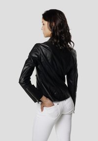 Čierna kožená bunda s priliehavým strihom, viditeľné švy a rukávy so zipsom, nosená s bielymi džínsami, čím sa zdôrazňuje kontrast farieb a textúr.