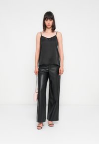 Camisole en satin noir avec un col en perles, associé à un pantalon large taille haute en simili cuir. Les accessoires comprennent un petit sac rose et des sandales à lanières.