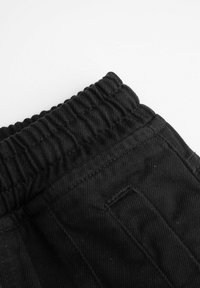 Czarny elastyczny pas materiałowych spodni z widocznym ściegiem i lekką teksturą. Zawiera detal kieszeni po bokach.