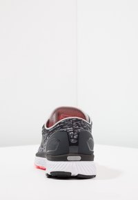 Scarpa da corsa nera e grigia con tomaia in maglia testurizzata, interno rosso, tallone rinforzato e suola intermedia bianca con accenti rosa.