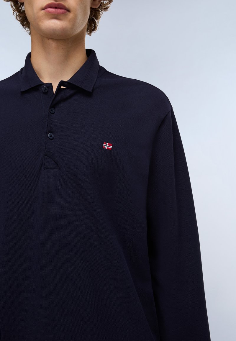 Navyblaues Langarm-Polohemd aus strukturiertem Stoff, mit einem Kragen und drei Knöpfen. Kleines Emblem mit einem rot-weißen Design auf der Brust.