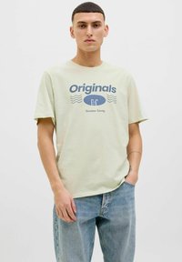 Lichtgroene katoenen t-shirt met "Originals" grafiek in marineblauw, met golvende lijnen en tekst. Korte mouwen, comfortabele pasvorm en ronde hals.