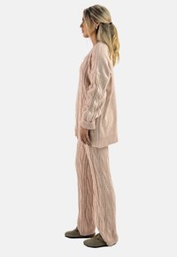 Zachte roze kabelgebreide trui met lange mouwen en bijpassende broek. De broek heeft een gestructureerd patroon en een wijd silhouet. Schoeisel in olijfgroen.