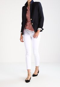 Marineblazer mit goldenen Knöpfen, rot-weiß gestreiftes Hemd, weißer schmaler Schnitt Hose und schwarze Ballerinas mit Schnürsenkeln.