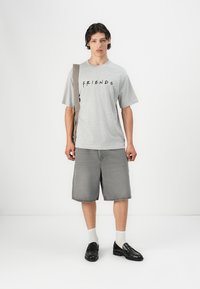 Grå T-shirt med kort ærme og "FRIENDS" tekst, parret med grå shorts til knæene. Hvide sokker og sorte loafers fuldender looket.