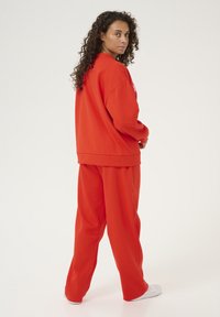 Rode oversized sweatshirt en bijpassende broek, gemaakt van zachte stof, met een relaxte pasvorm en een eenvoudig ontwerp. Witte schoenen maken de look compleet.