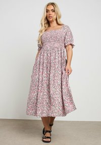 Ruusuinen midi-mekko vaaleanpunaisena, jossa on kiristettävä rintaosa ja puffihihoja. Mekossa on eläväinen kuvio pienistä vihreistä ja mustista kukista.