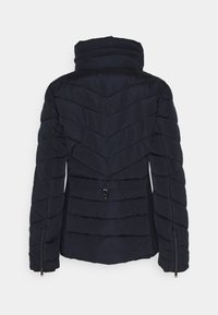 Chaqueta negra acolchada con cuello alto, patrones de costura horizontales y en chevron, y puños con cremallera vista desde atrás.