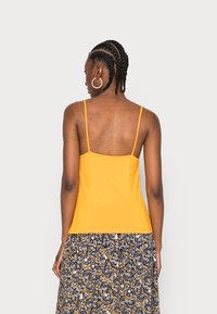 Camisola amarela com alças finas, combinada com uma saia floral estampada com detalhes em azul, branco e amarelo. Textura de tecido suave.