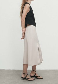 Black sleeveless top, pale pink midi skirt with a front slit, and black flat sandals with ankle straps, set against a neutral background.